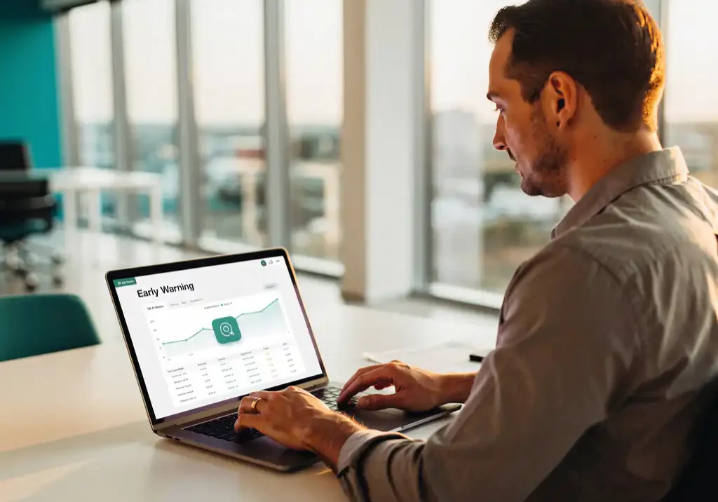 HR-manager bekijkt vroegwaarschuwingsdashboard op laptop in licht modern kantoor met warm natuurlijk licht.